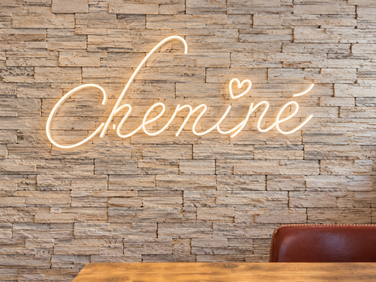 Illuminated Cheminé sign on the café’s stone wall, with a burgundy chair and wooden table