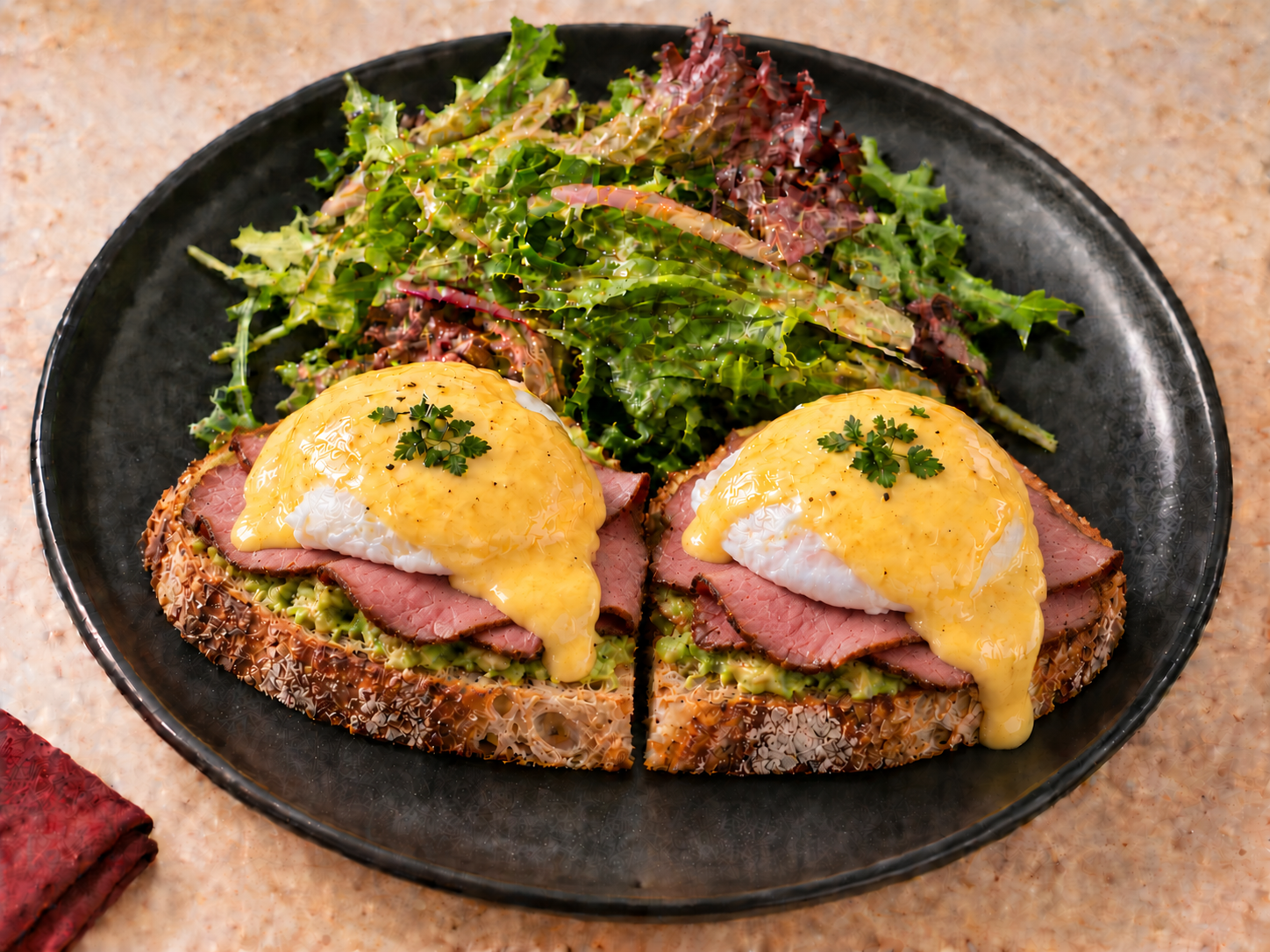 CHEMINÈ Smoked Beef Eggs Benedict with hollandaise and mixed greens on a black plate