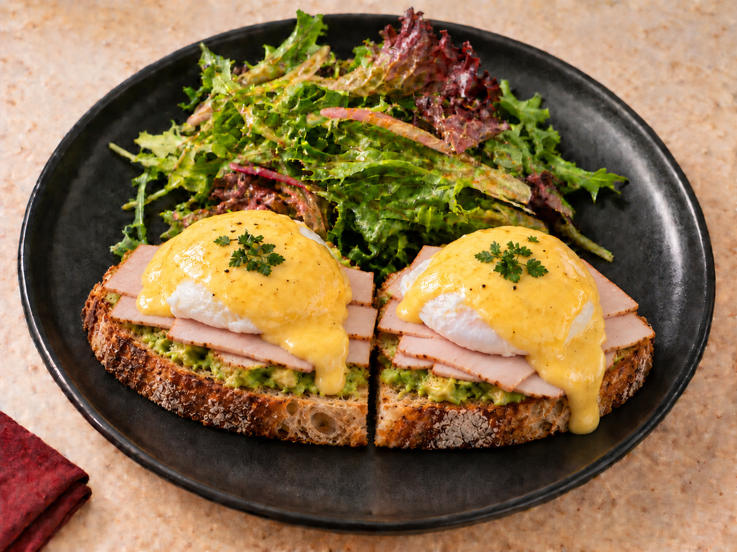 CHEMINÈ Smoked Turkey Eggs Benedict with avocado on sourdough, hollandaise, and mixed greens on a black plate