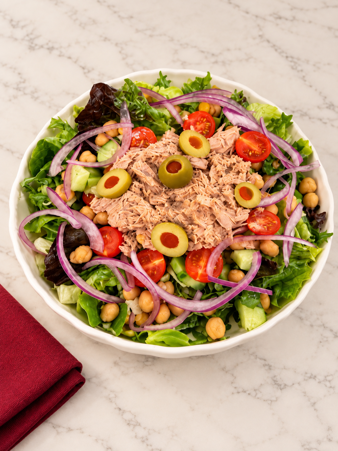 CHEMINÈ Mediterranean Tuna Salad in a white bowl on marble with a burgundy napkin